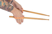Child holds drumsticks with the help of an orange assitive device silicone strap.
