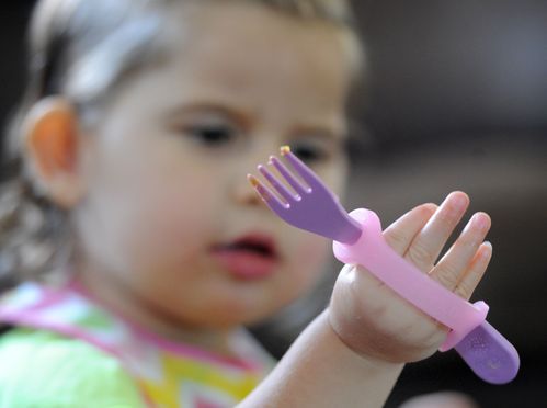 Pediatric size pink silicone grip aid on a childs hand and fork.