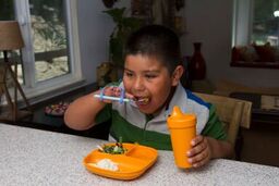 Child gripping a special needs blue silicone eating utensil.