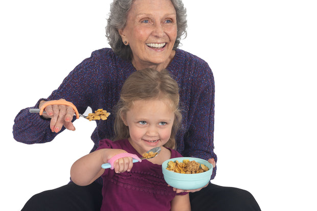 Mom with arthritis and child with pediatric arthritis hold spoons with the eazyhold silicone assistive devices gripped on their hands.
